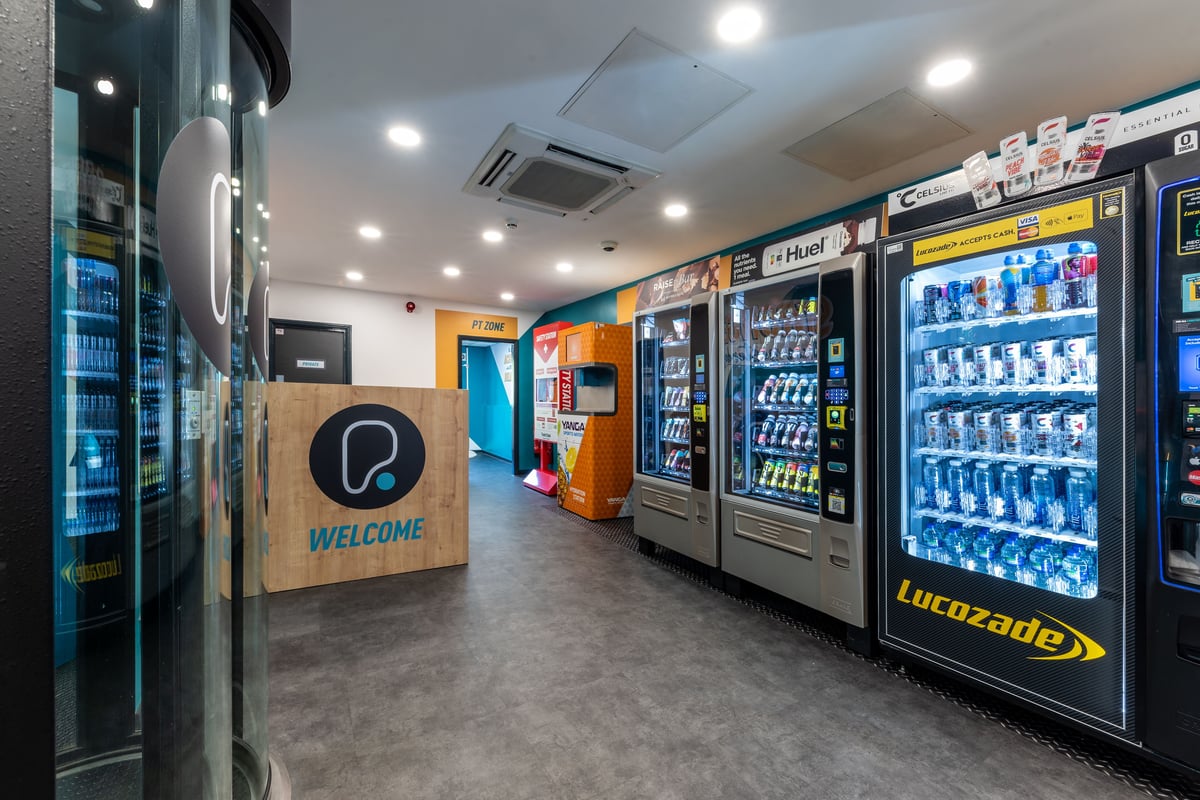 PureGym London Muswell Hill: Refrigerated vending machines stocked with beverages and snacks in a small lobby area.
