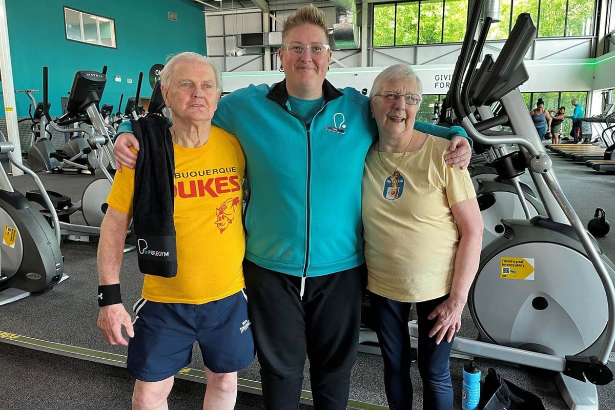 Three people standing with arms around each other in a gym with exercise machines