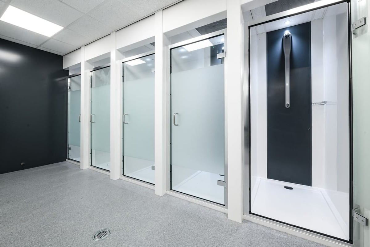 PureGym Leeds Thorpe Park: Rows of frosted glass doors and shower stalls, typical of a changing room facility.