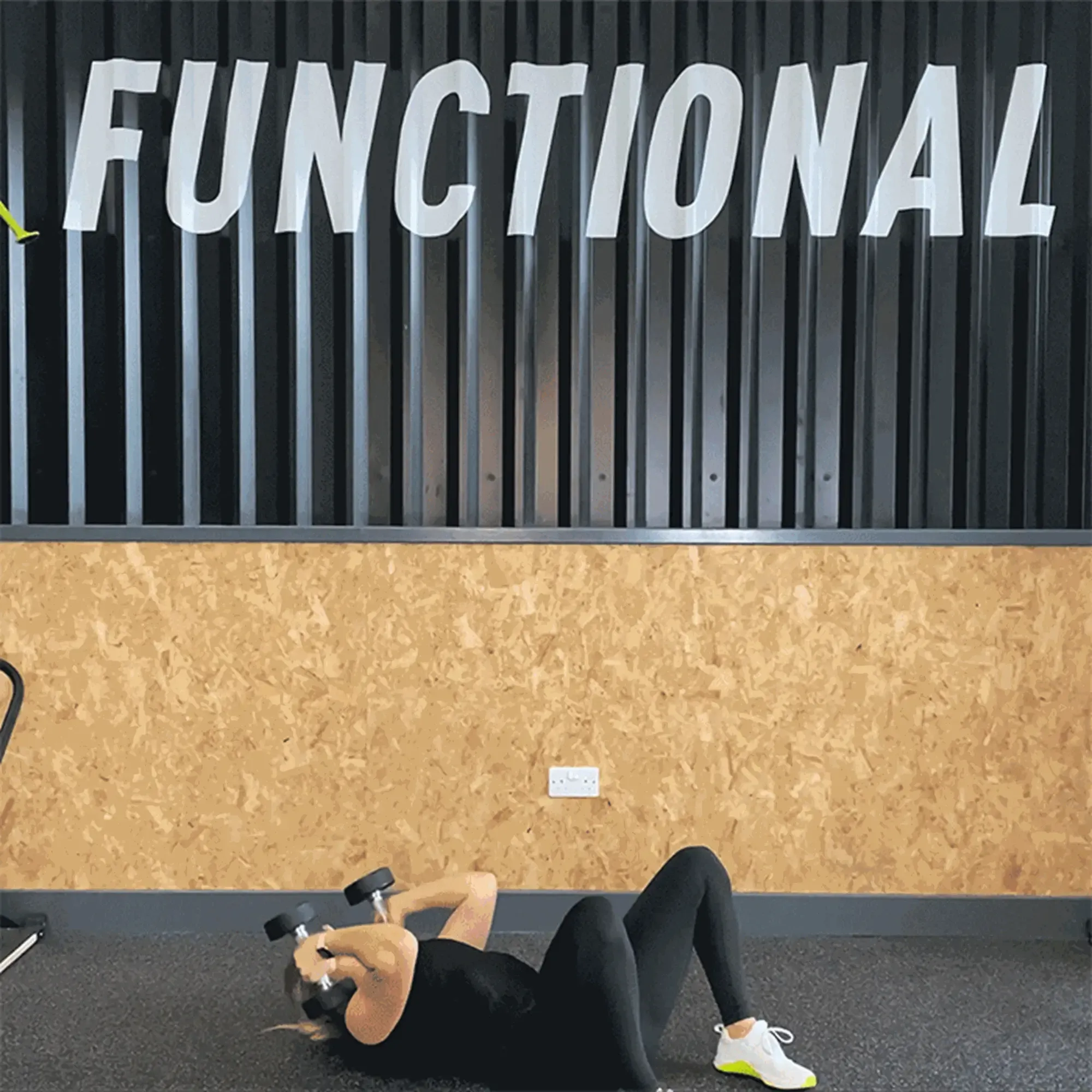 Person lying on floor lifting dumbbells in gym with functional sign above