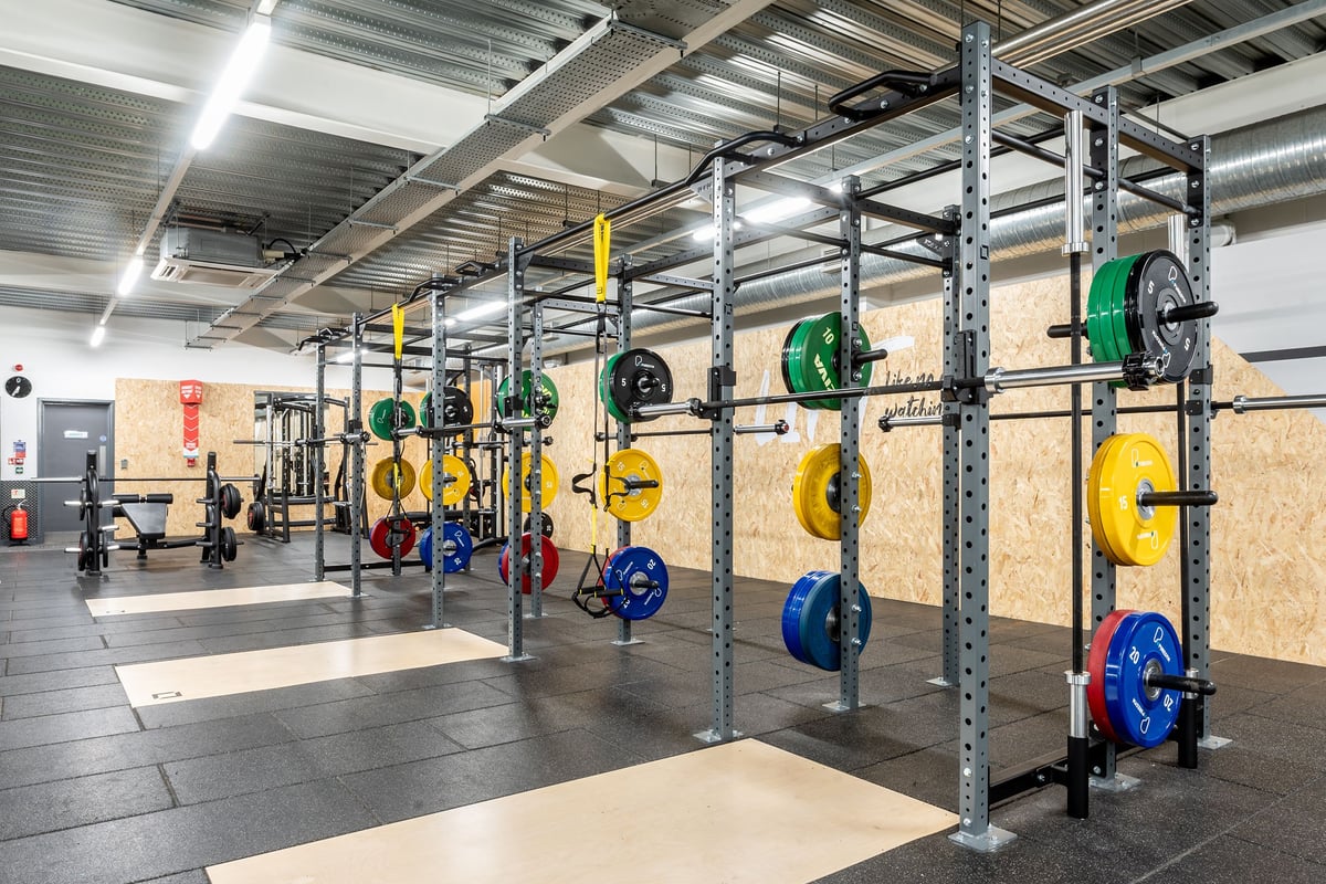 PureGym Banbury Cross Retail Park: Squat racks with weight plates in bright colours sit spaced out in a training area.