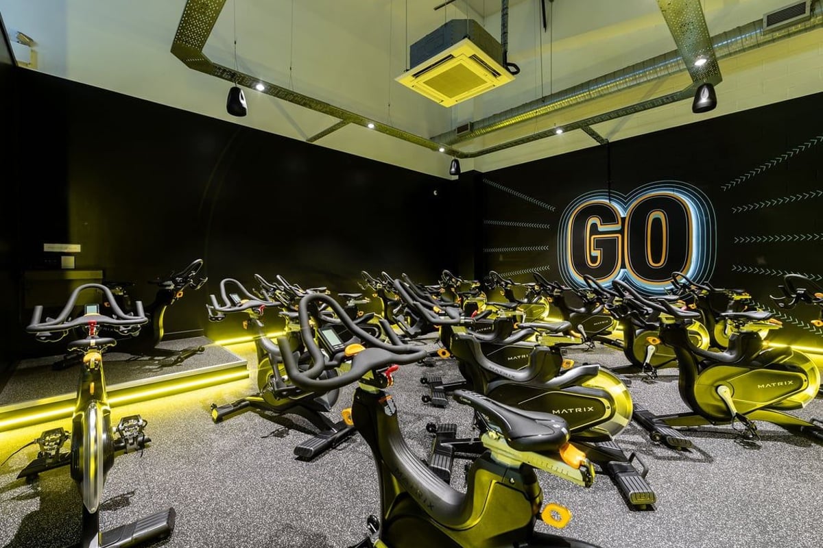 PureGym Banbury Cross Retail Park: Spin bikes arranged in rows with yellow lighting and a large "GO" sign on the wall.