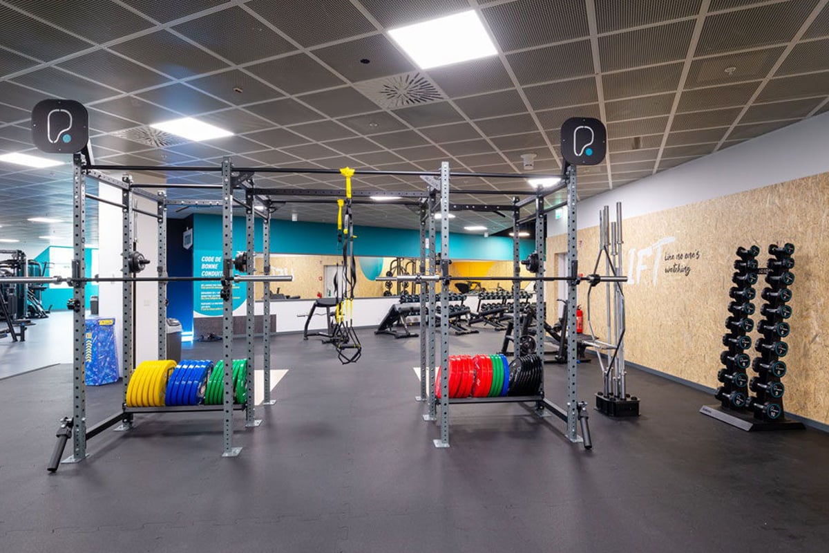PureGym Lausanne Prilly: Workout area with rig, weights, benches, and rubberized flooring in bright colours.