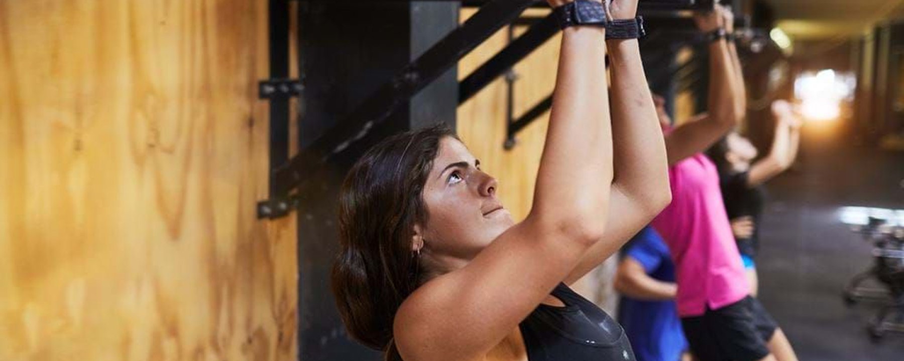 Women doing pull-ups on a metal bar in a gym with wooden and brick walls