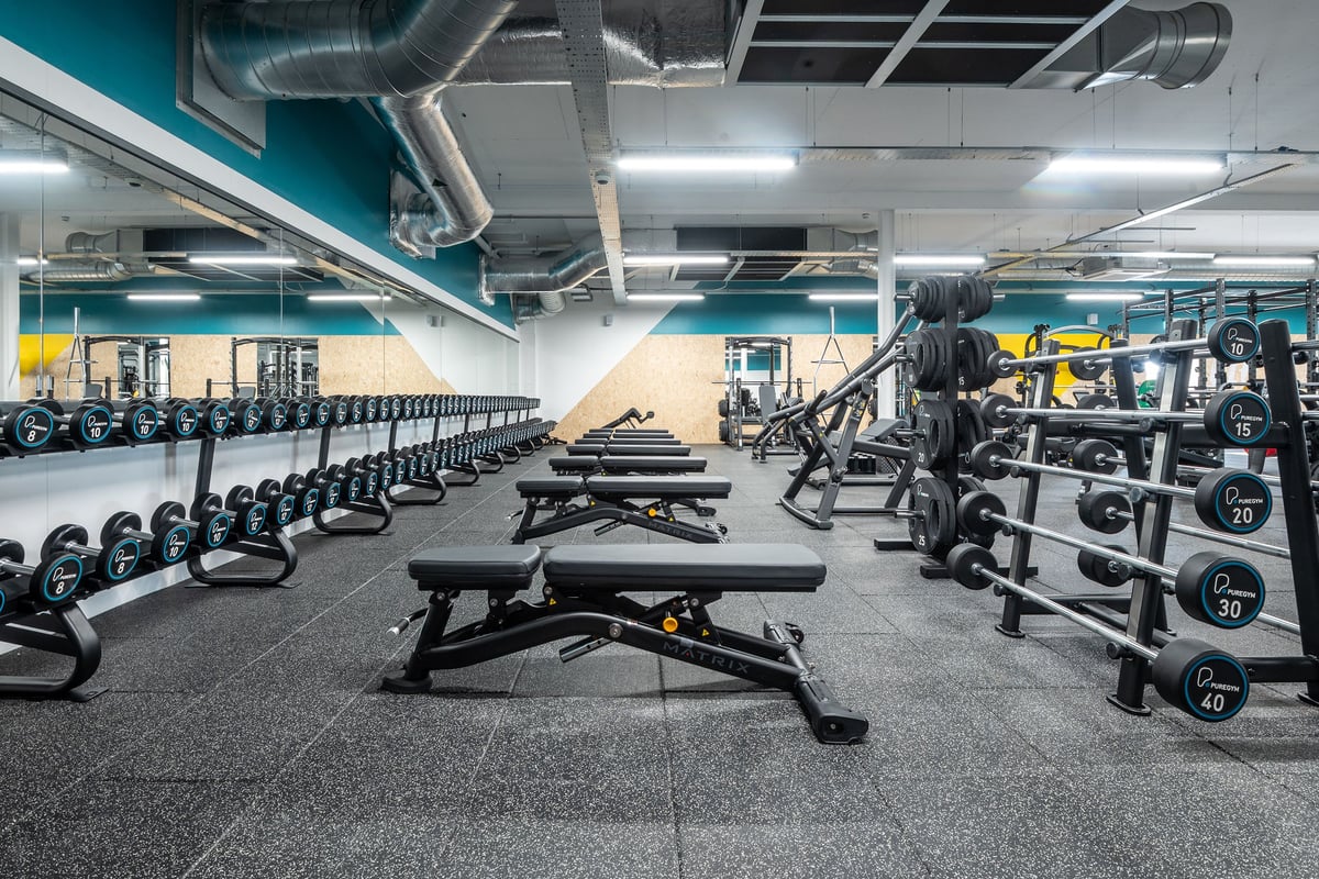 PureGym Glasgow Rutherglen: Rows of benches, free weights, squat racks, and weight plates on rubberized flooring.