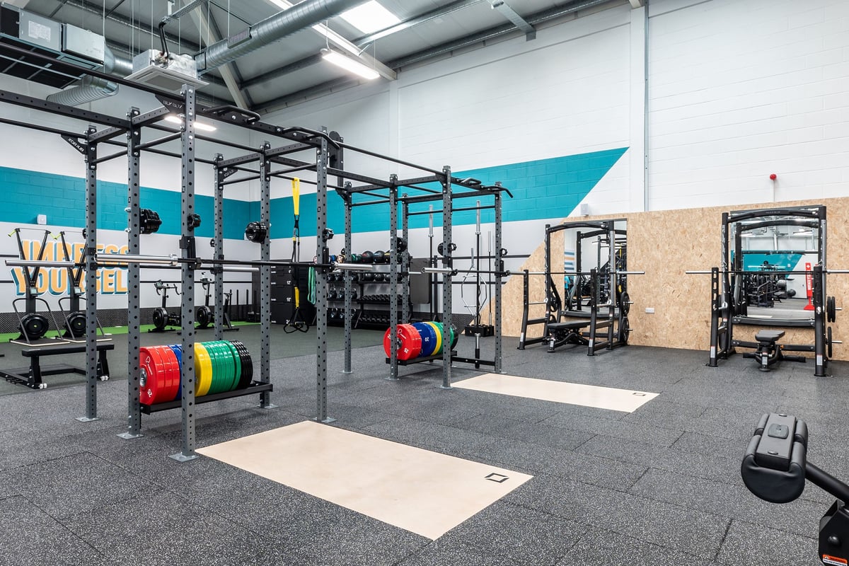 PureGym Dumfries: Rigging racks, weight plates, rubberised mats, and functional training equipment inside a fitness studio.