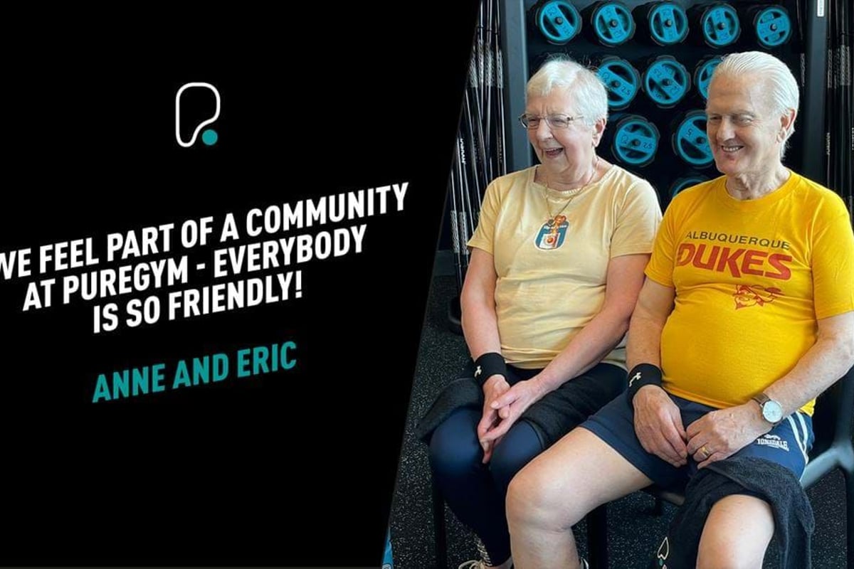 Two elderly people sitting and smiling in a gym with weights in the background