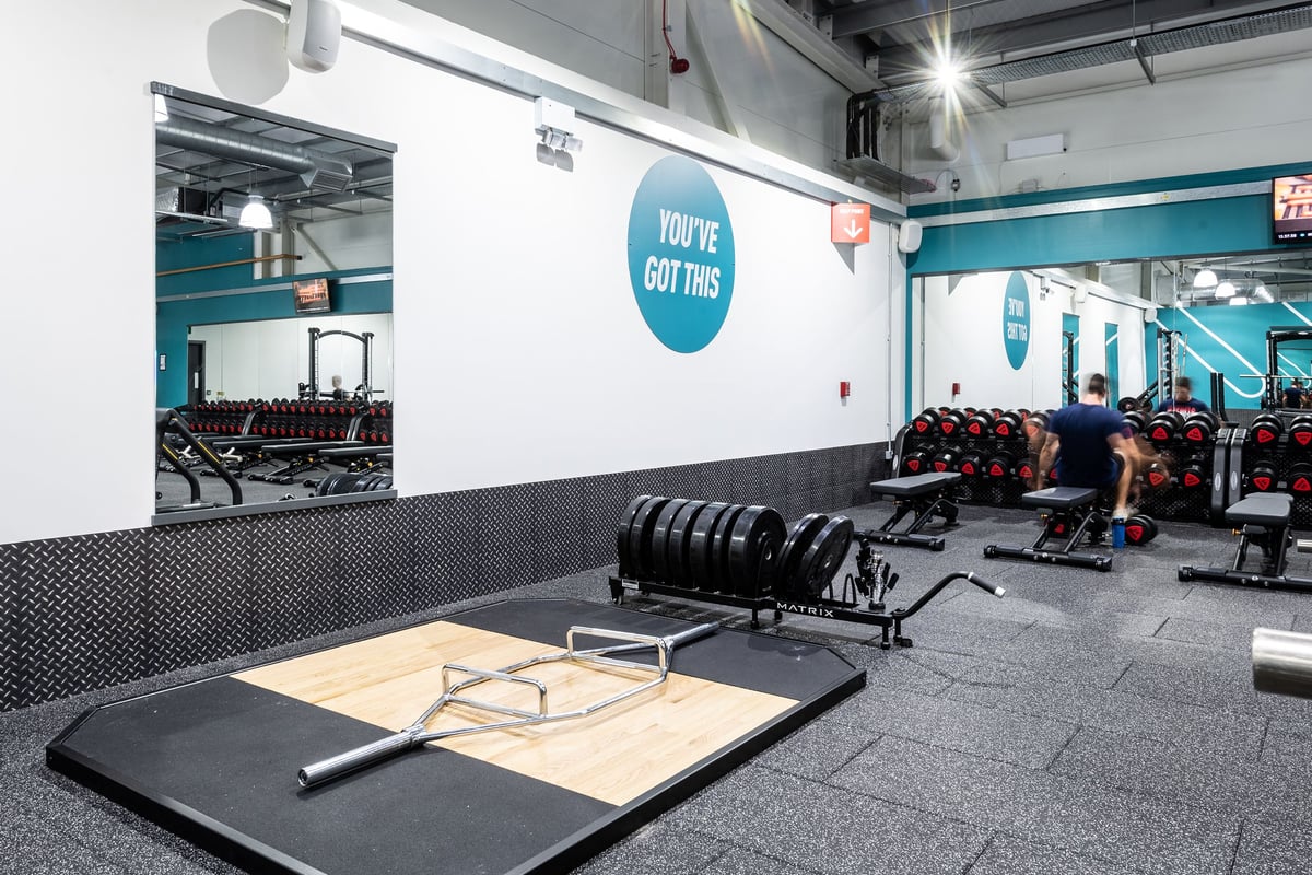 PureGym Portsmouth North Harbour: Weight sleds, benches, mirrors, rubberized flooring in teal and grey color scheme.