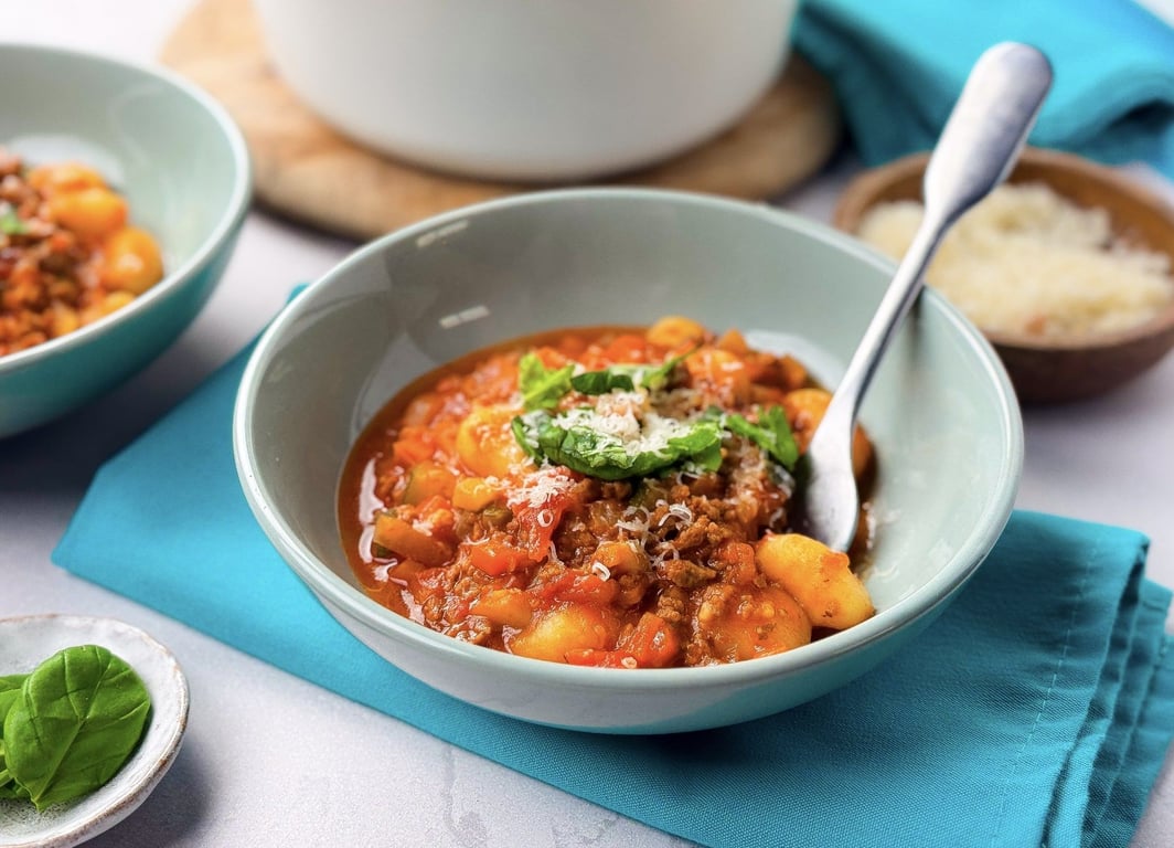 Bowl of gnocchi in tomato sauce with grated cheese and basil on a blue napkin