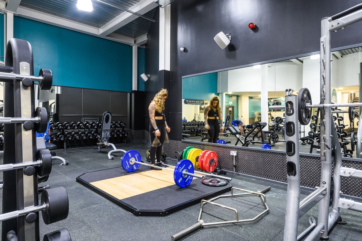 PureGym London Wandsworth: Strength training area with squat racks, weight plates, dumbbells, benches, rubberized flooring.