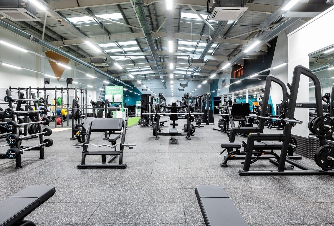 PureGym Ashford Warren Retail Park: Gym interior with weight machines, benches, rubberized flooring, and mirrored walls.