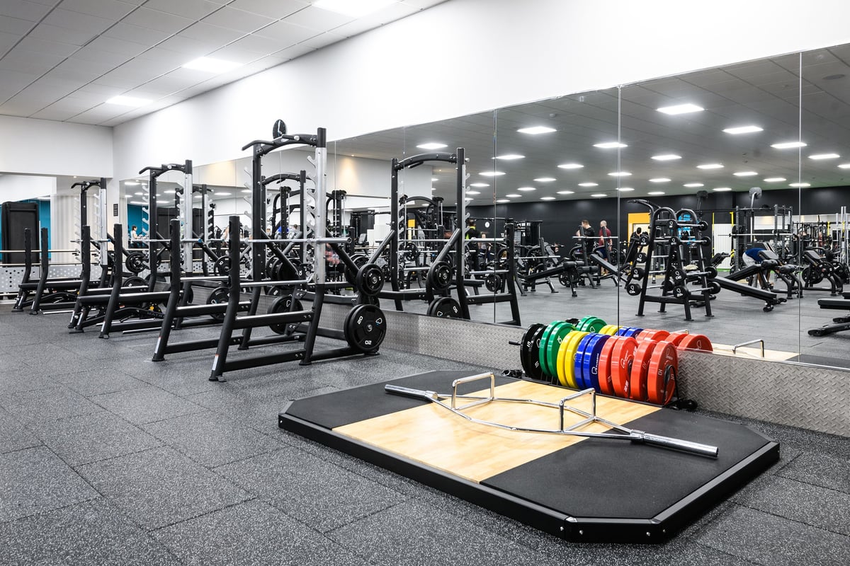 PureGym Aylesbury: Squat racks, weight plates of various colours, rubberized flooring, and weightlifting platforms.