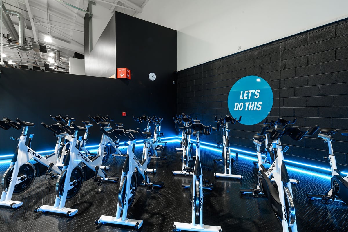 PureGym Exeter Bishops Court: Rows of stationary cycling machines illuminated in blue lighting, with motivational signage on the wall.