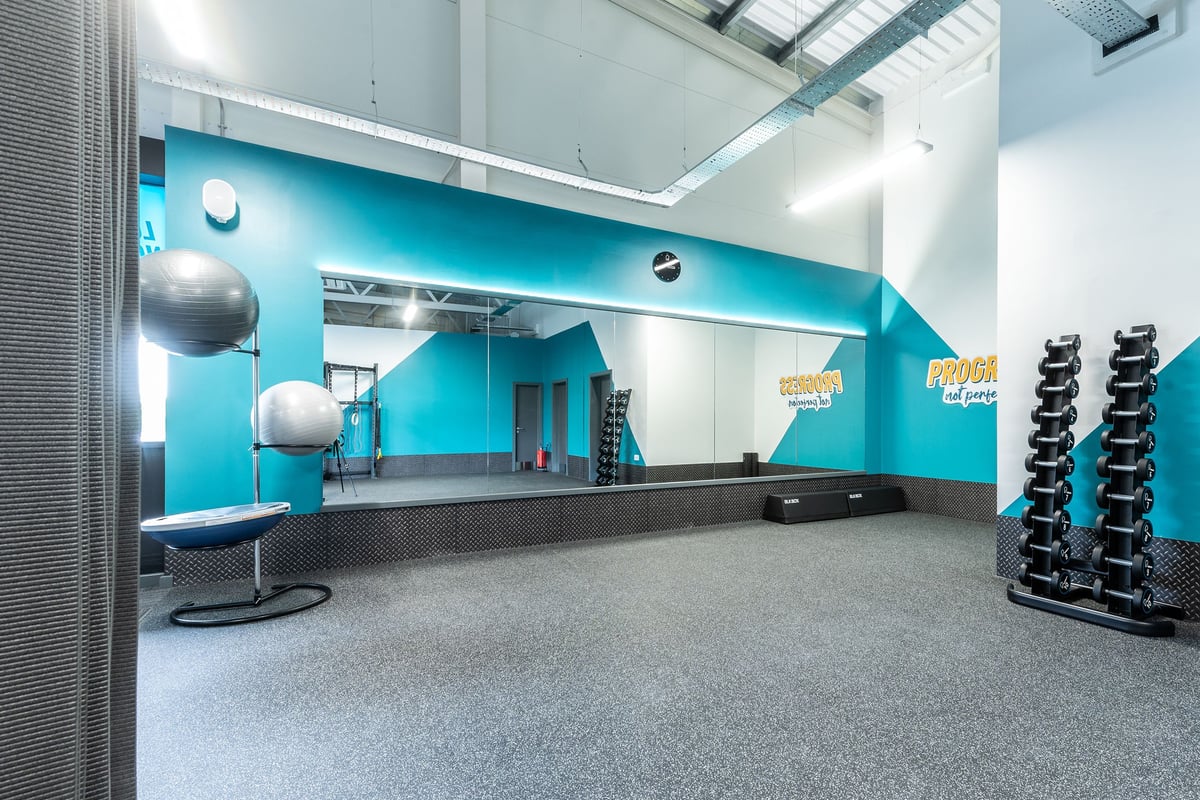 PureGym Barnsley: Mirrored studio with medicine balls, free weights, rubberized floors, and teal accent walls.