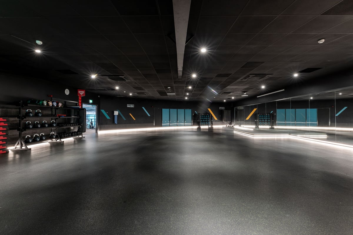 PureGym Brierley Hill: Large mirrored studio space with dim lighting, rubberized floors, free weights area.