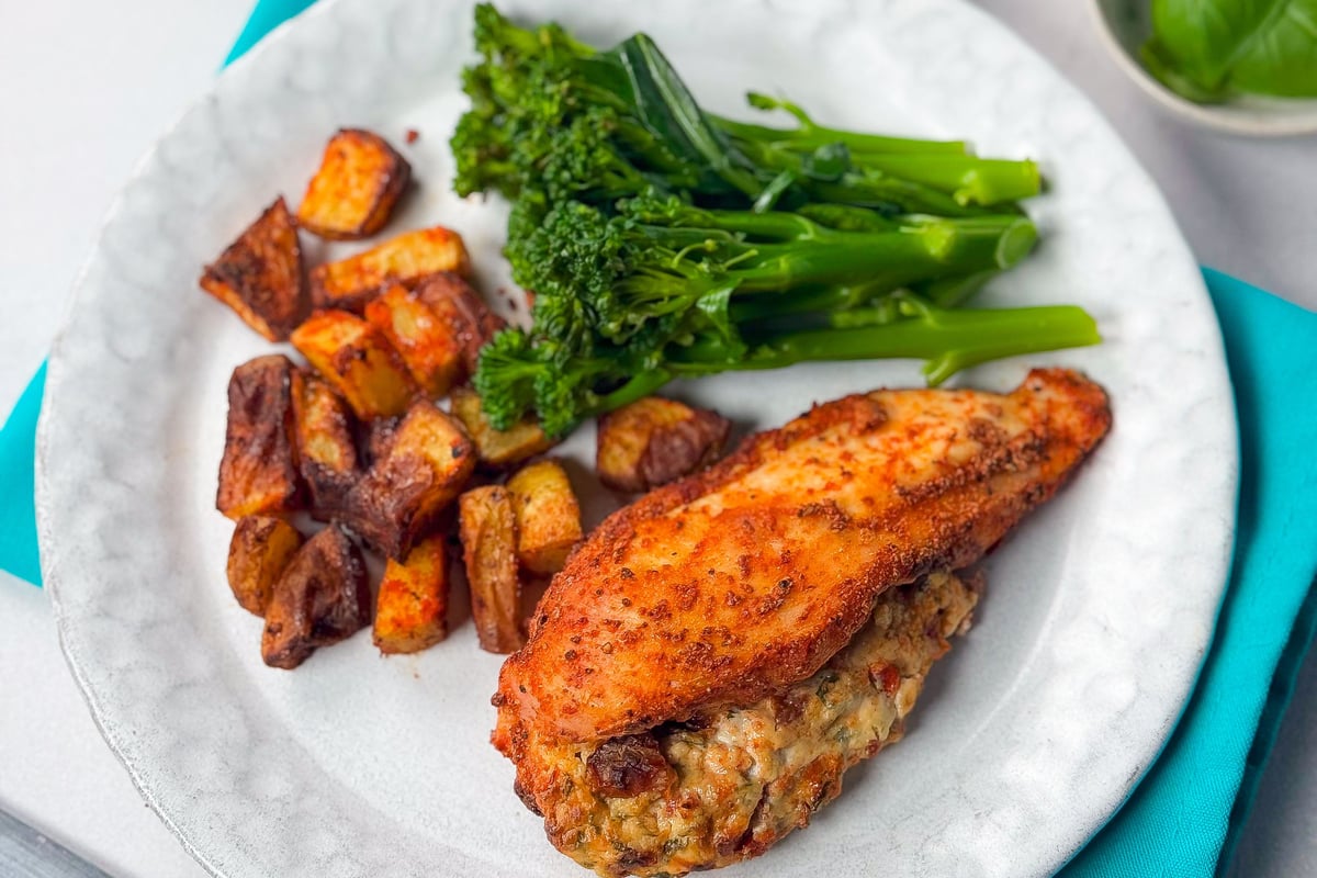 Stuffed chicken breast with roasted potatoes and steamed broccolini on a white plate