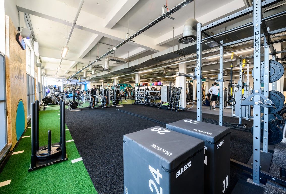 PureGym London Camden: Strength training area with squat racks, weight plates, turf sections, rubberized floor.