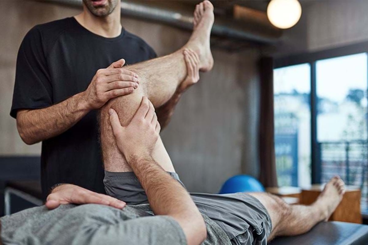 Physiotherapist stretching a man's bent leg on a treatment table in a clinic.