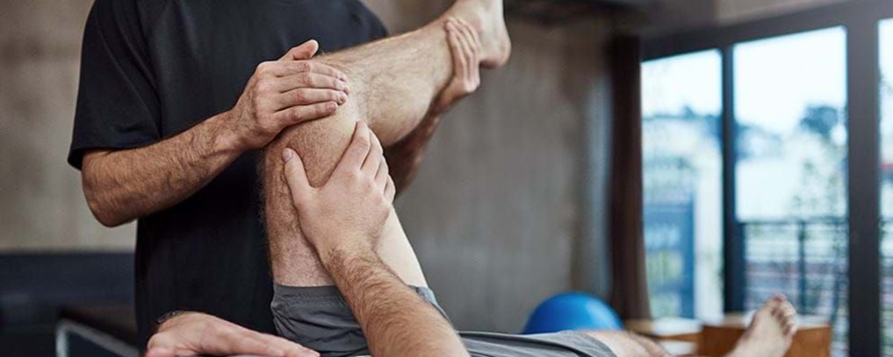 Physiotherapist stretching a man's bent leg on a treatment table in a clinic.