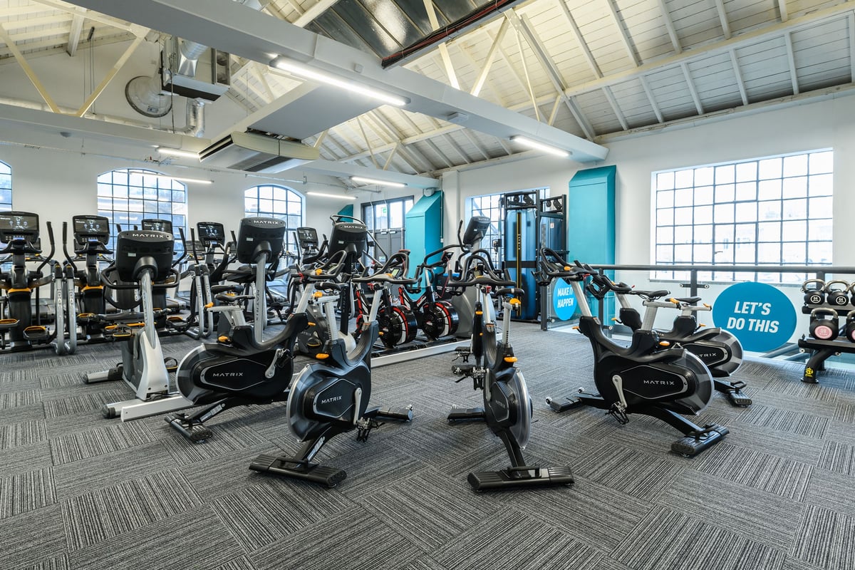 PureGym London Bow Wharf: Rows of stationary bikes, treadmills, weight machines, and mirrored walls in a bright gym interior.