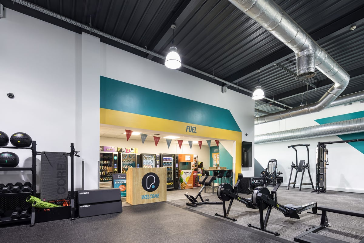 PureGym Dudley Tipton: Rows of exercise machines, free weights, and a colourful front desk area with geometric designs.