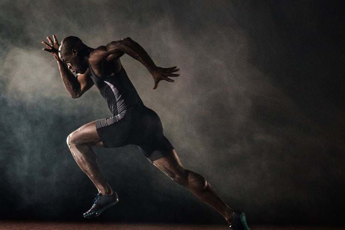 Male sprinter in black sportswear running on a track with smoke in the background