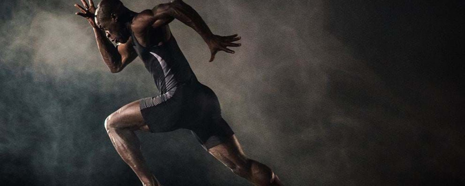 Male sprinter in black sportswear running on a track with smoke in the background