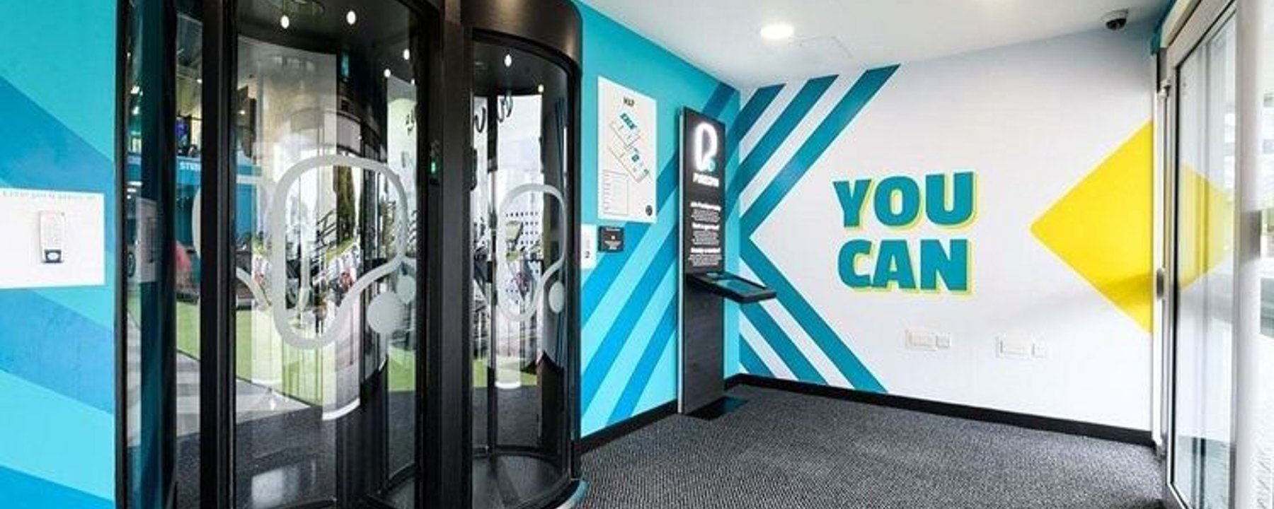 Modern entrance with two black revolving doors and a wall sign saying YOU CAN