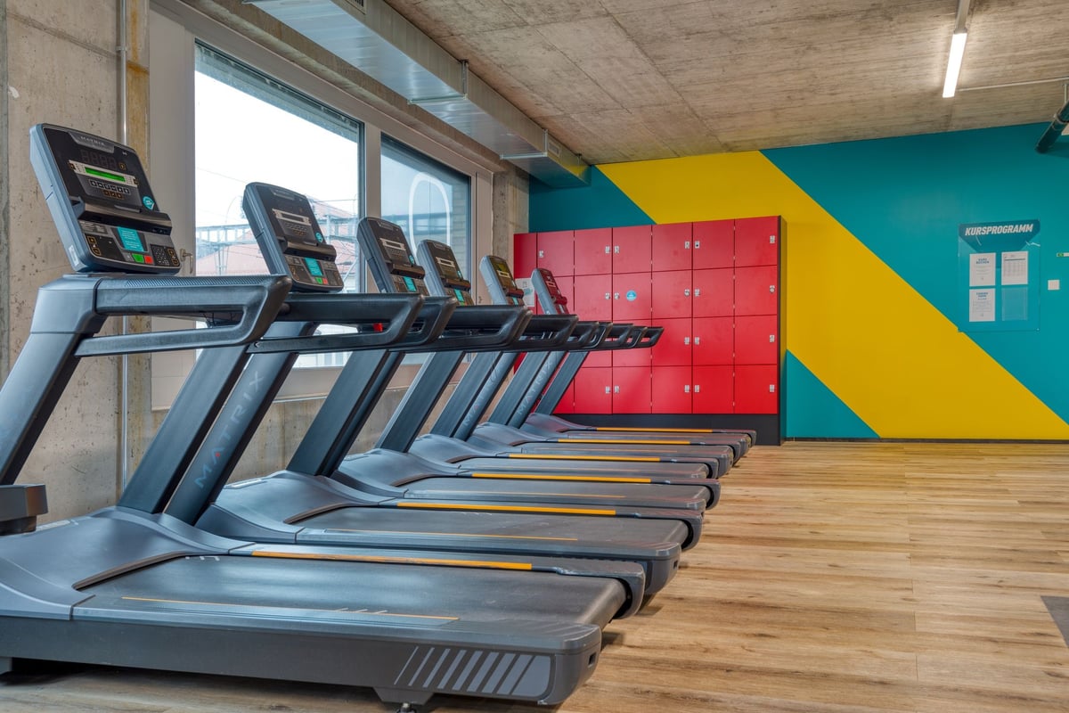 PureGym Lenzburg : des rangées de tapis de course dans une salle de sport avec des accents muraux colorés et