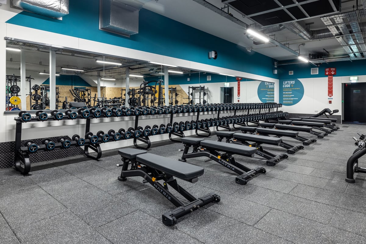 PureGym Hull Clough Road: Rows of free weight benches, dumbbells, and weight racks in a teal and white gym studio.