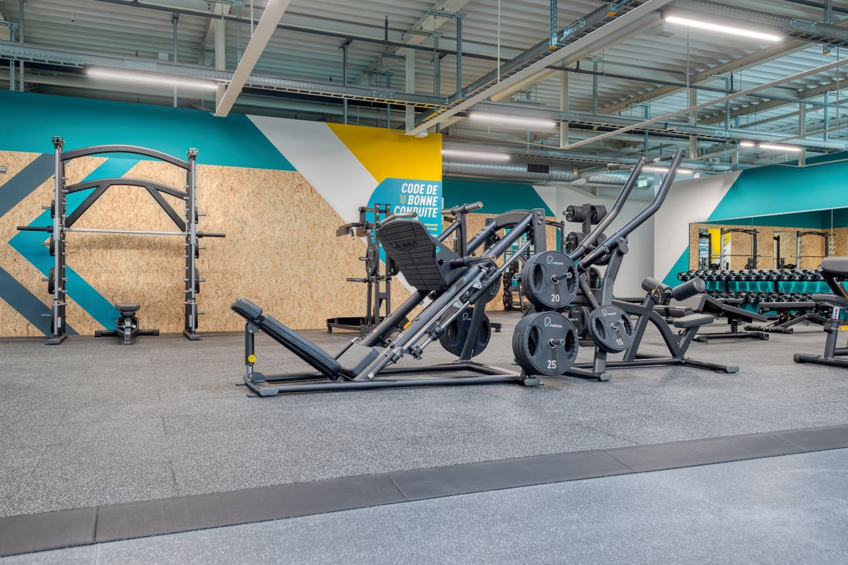 PureGym Martigny: Reihenweise Trainingsgeräte wie Kabelgeräte, Bänke und Hockstützen auf gummiertem Fitnessboden.