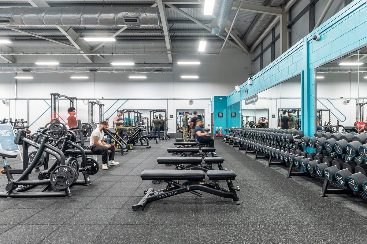 PureGym Birmingham West: Large gym studio with rows of weight machines, free weights, benches, and rubberized flooring.