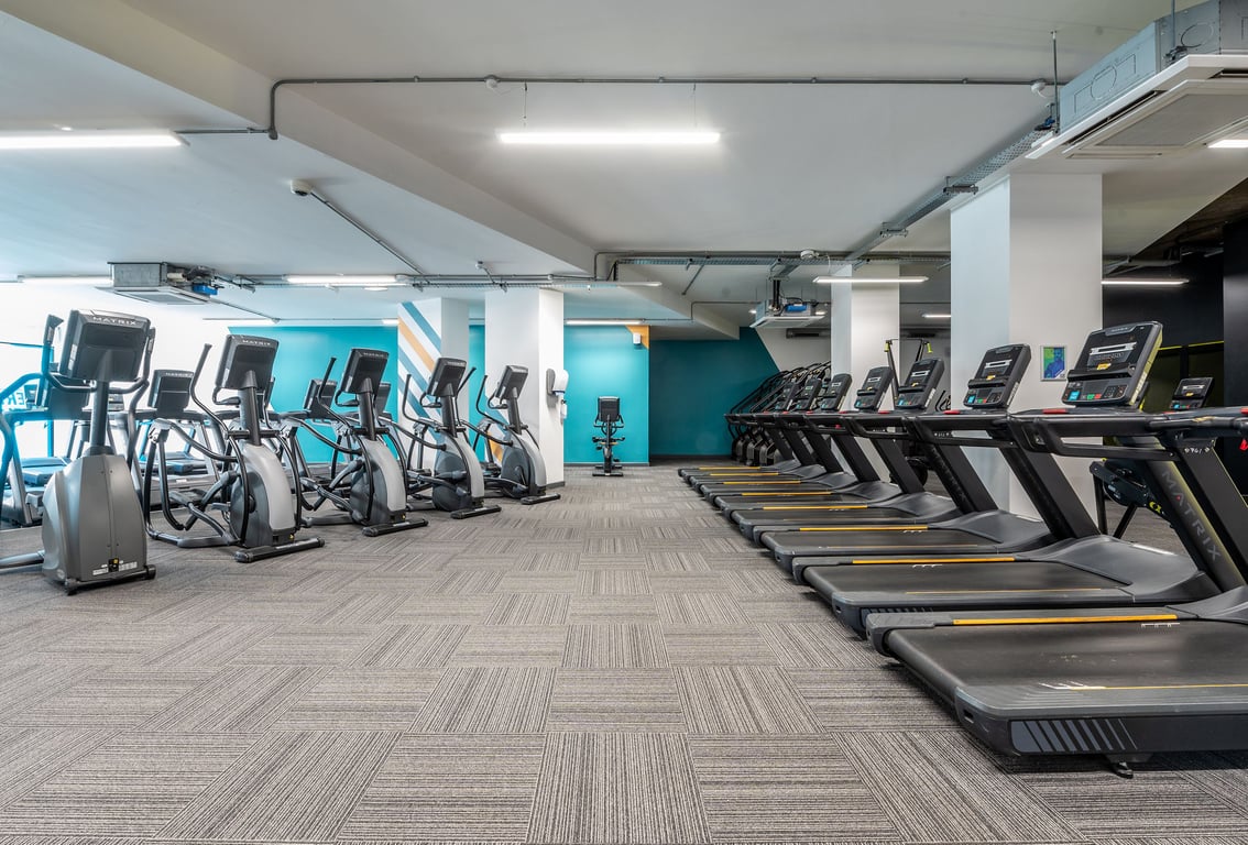 PureGym London Swiss Cottage: Rows of exercise bikes, treadmills, and a strength training area with rubberized flooring.