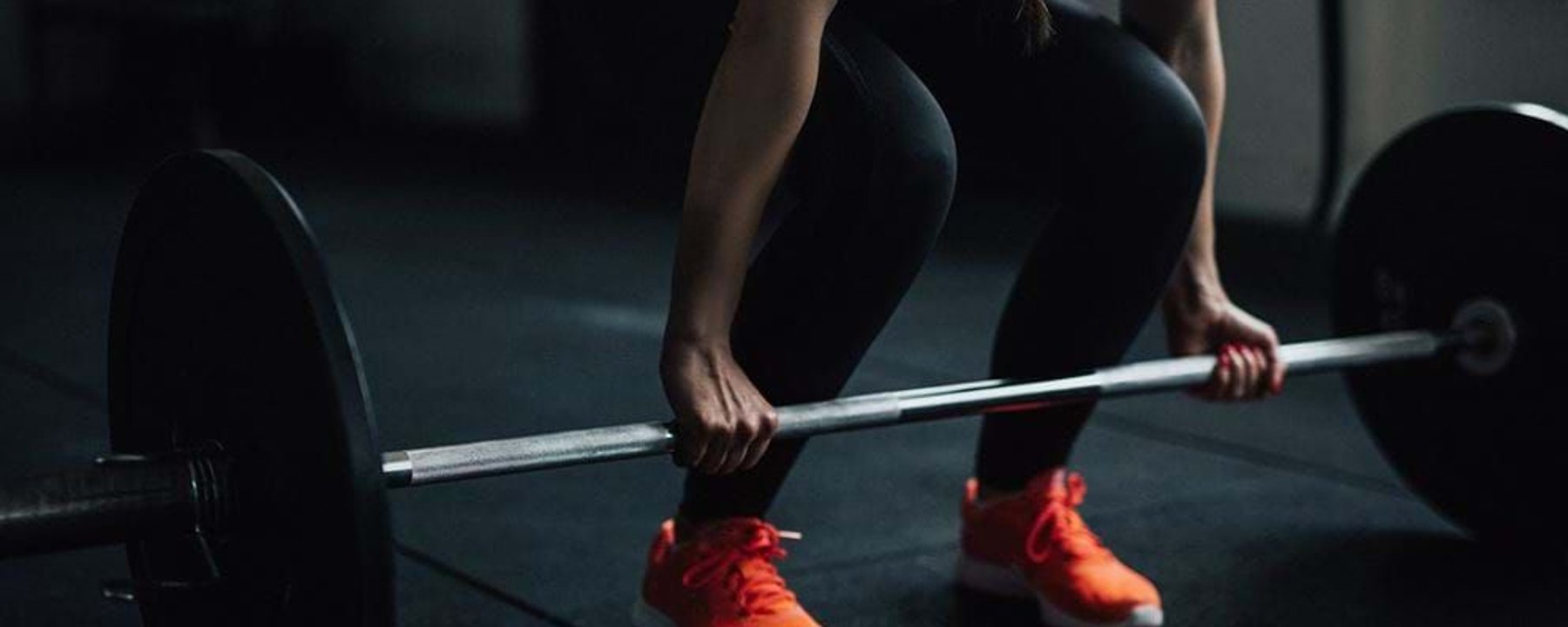 Person in black leggings and orange trainers lifting a barbell in a gym