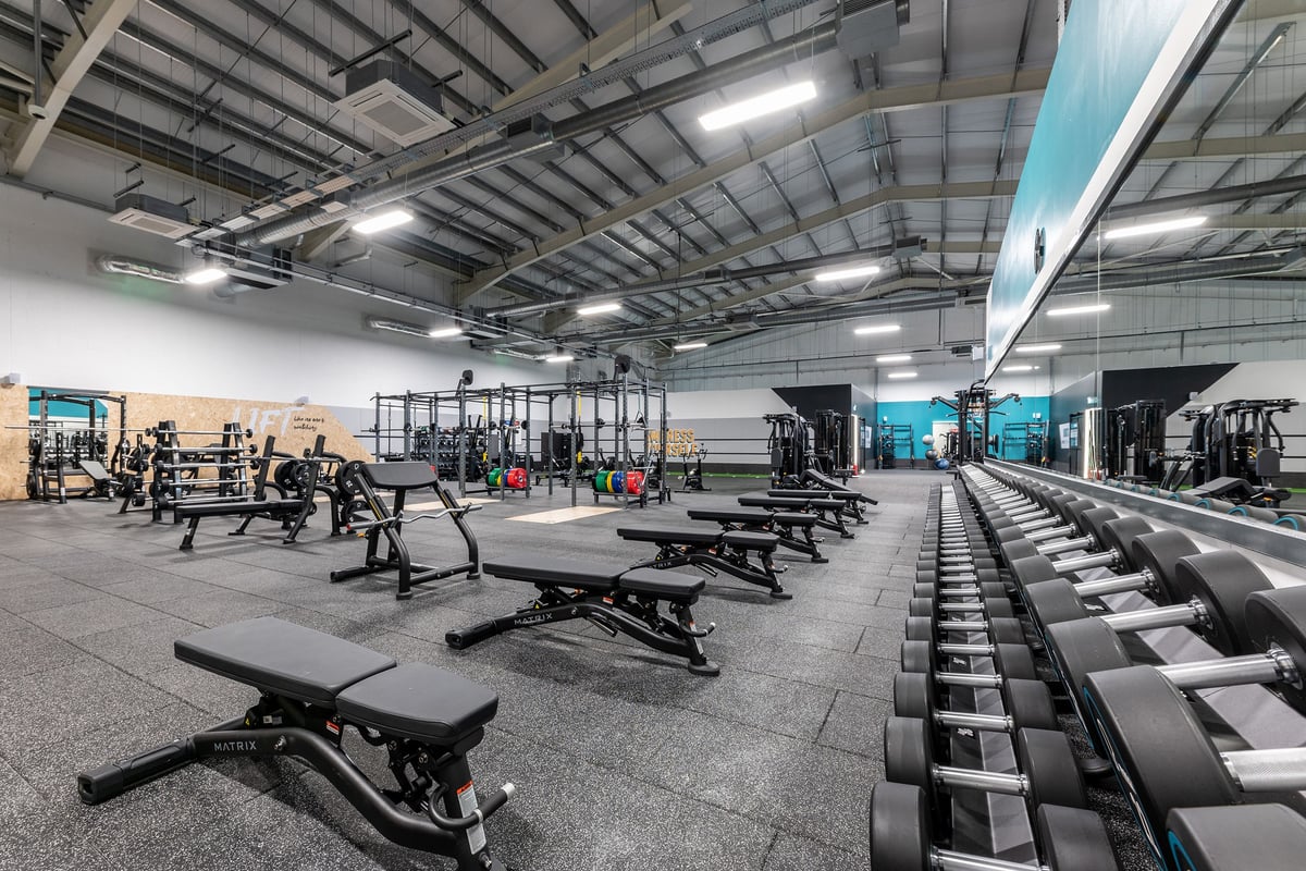 PureGym Lincoln Carlton Centre: Gym with weight benches, squat racks, free weights, rubberized flooring, and mirrored walls.