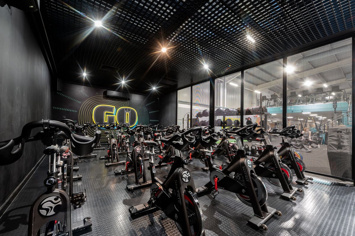 PureGym Southampton Central: Rows of stationary bikes, spin cycles amid dim lighting and perforated ceiling panels.