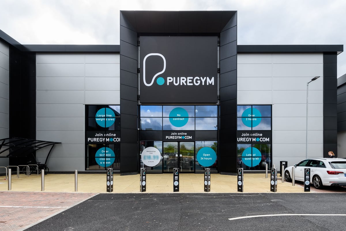 PureGym Lichfield: Puregym exterior with signage, frosted glass windows, parking spaces, and crowd control barriers.