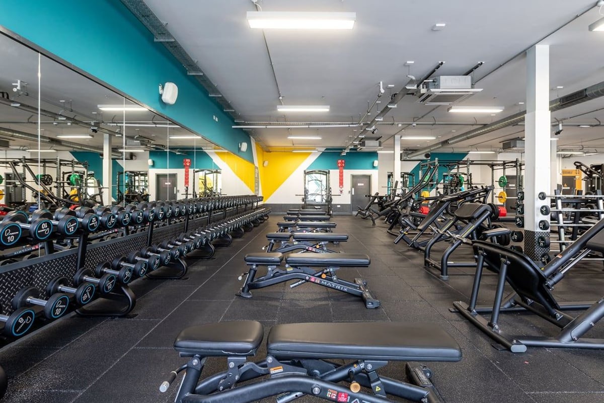 PureGym Wirral Bidston Moss: Rows of dumbbells, weight benches, resistance machines with turquoise and yellow accents.