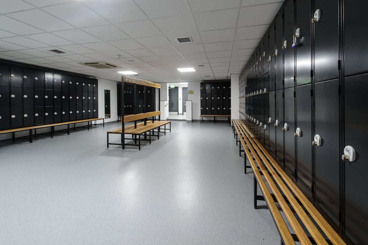 PureGym Bedford Heights: Rows of lockers, benches, and open space with fluorescent lighting.