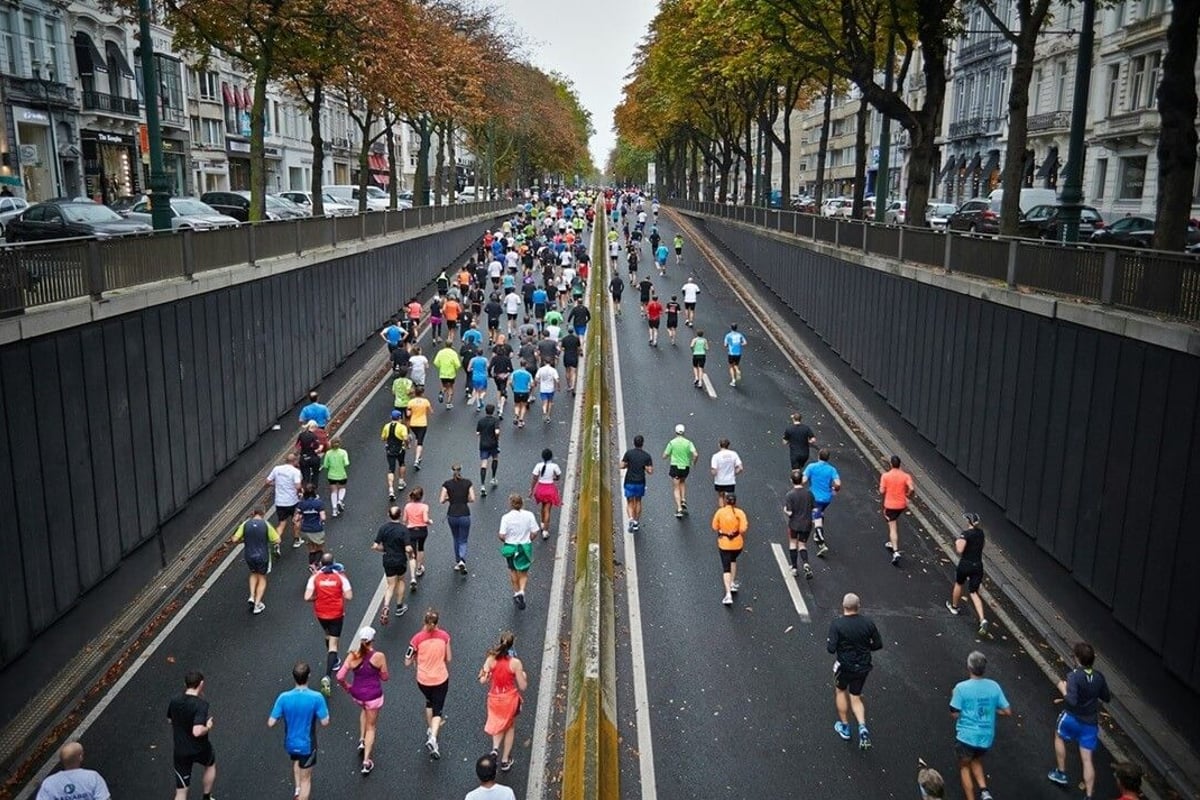 Marathon runners in colourful sportswear running along tree-lined city street in autumn