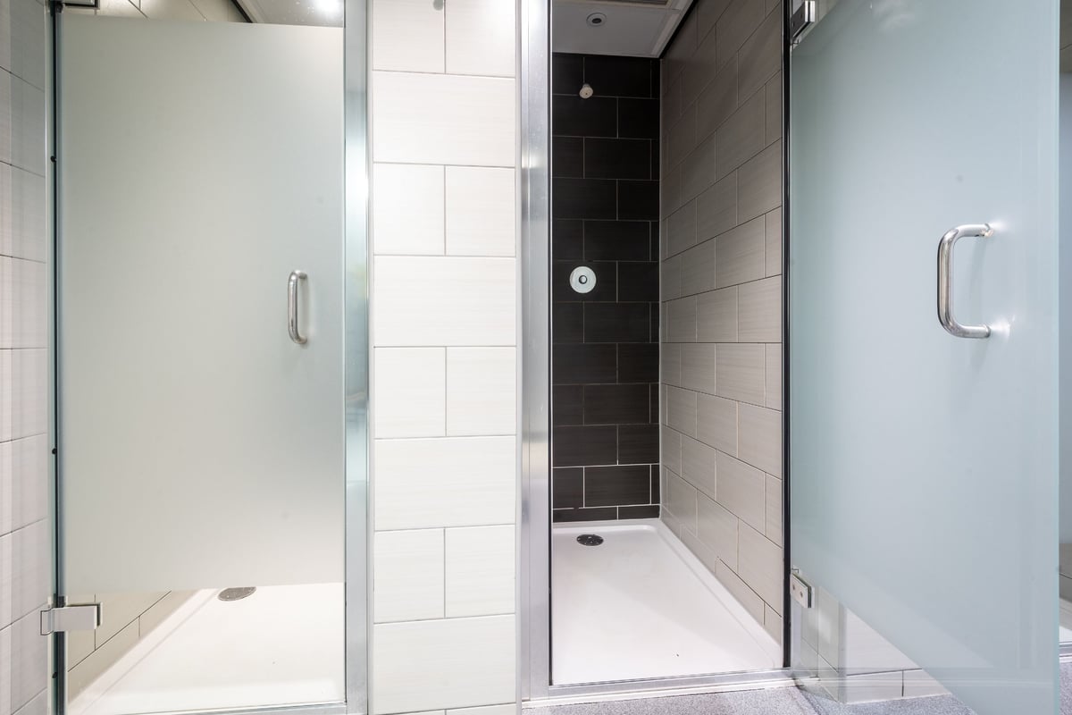 PureGym Edinburgh Exchange Crescent: Shower stall with glass doors, tiled walls, and modern fixtures.