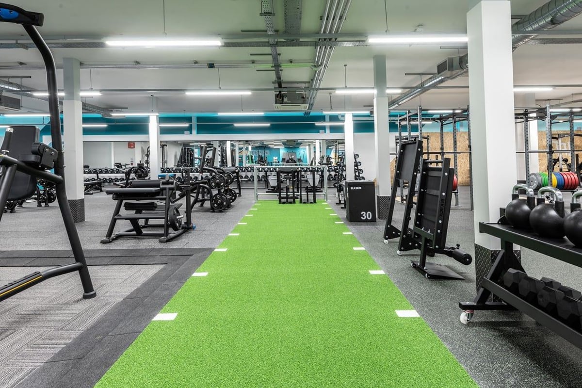 PureGym Milton Keynes Kingston Centre: Gym with free weights, weight machines, green turf area, and concrete pillars.