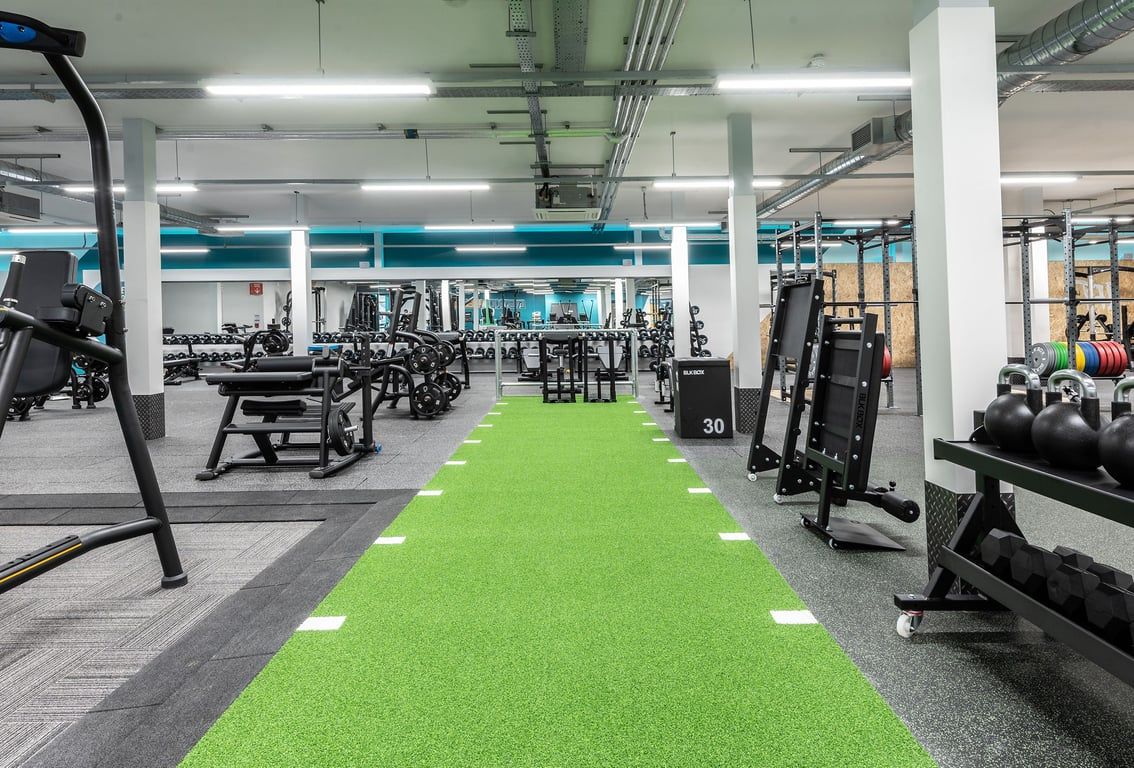 PureGym Milton Keynes Kingston Centre: Gym with free weights, weight machines, green turf area, and concrete pillars.