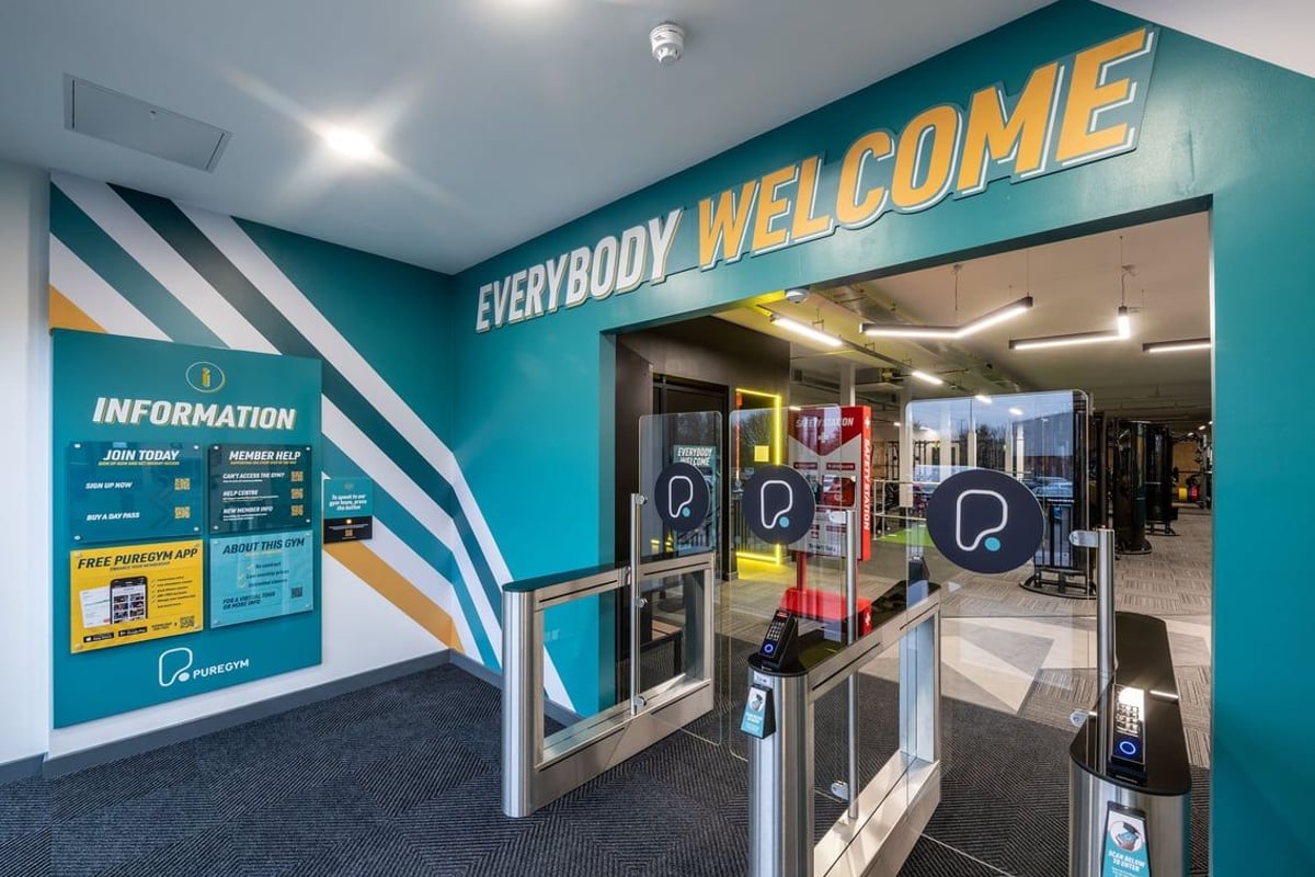 PureGym Derby Kingsway Retail Park: Entrance area with turnstiles, information signage, and "Everybody Welcome" wall mural.
