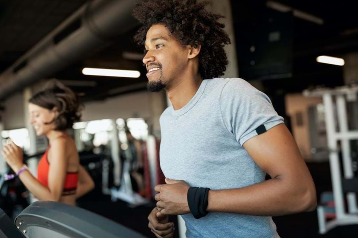 Two people running on treadmills in a gym with exercise equipment in the background