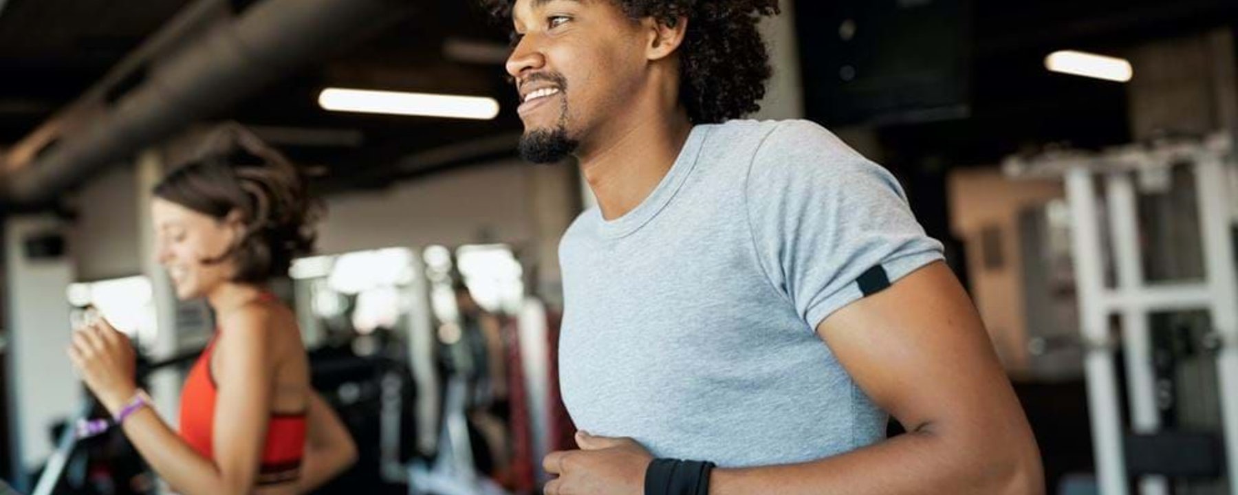 Two people running on treadmills in a gym with exercise equipment in the background