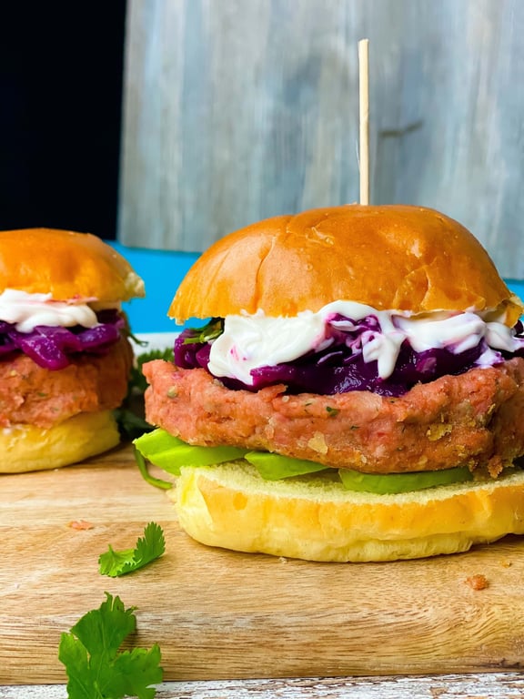 Two burgers with lettuce, purple cabbage, and white sauce on wooden board