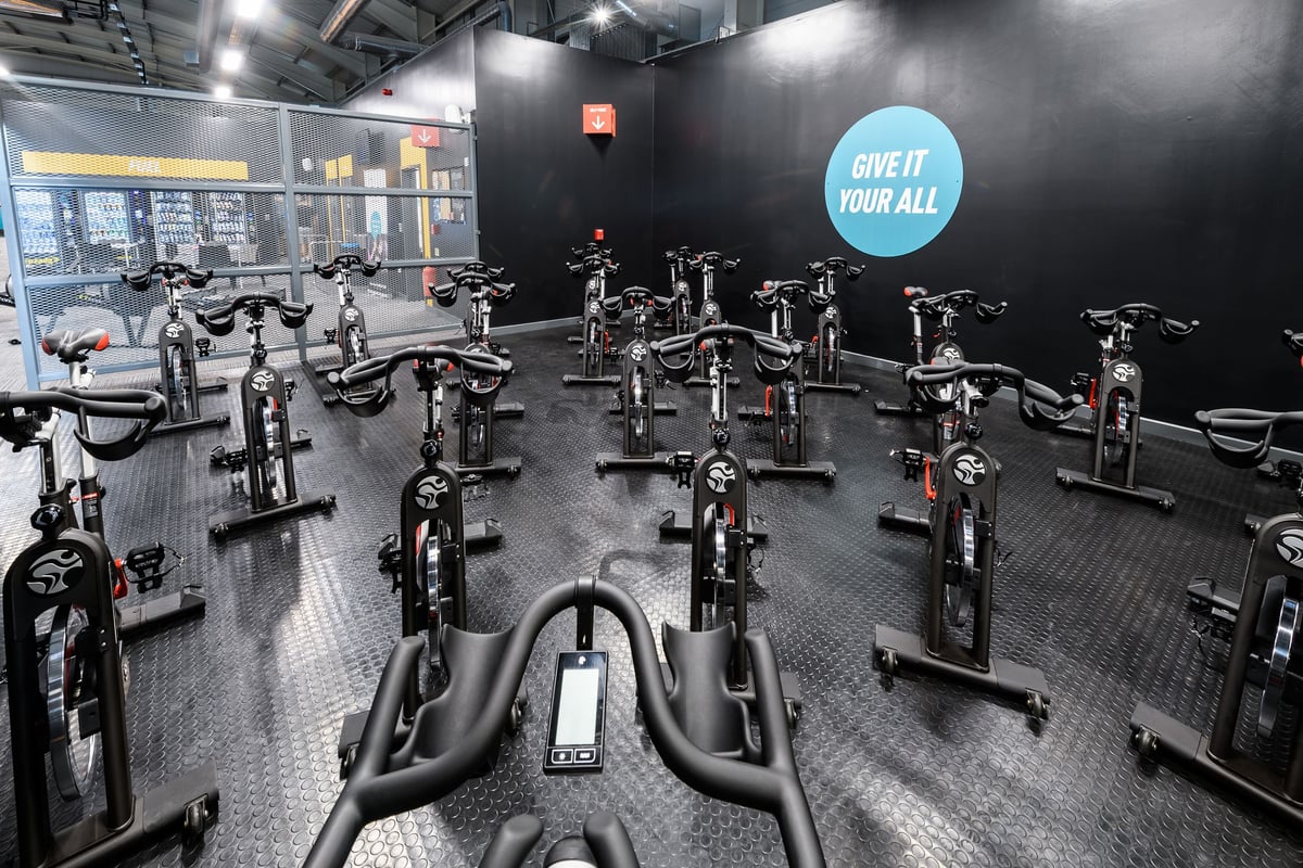 PureGym Fareham: Rows of stationary bikes with blue motivational signage on dark walls and industrial lighting.
