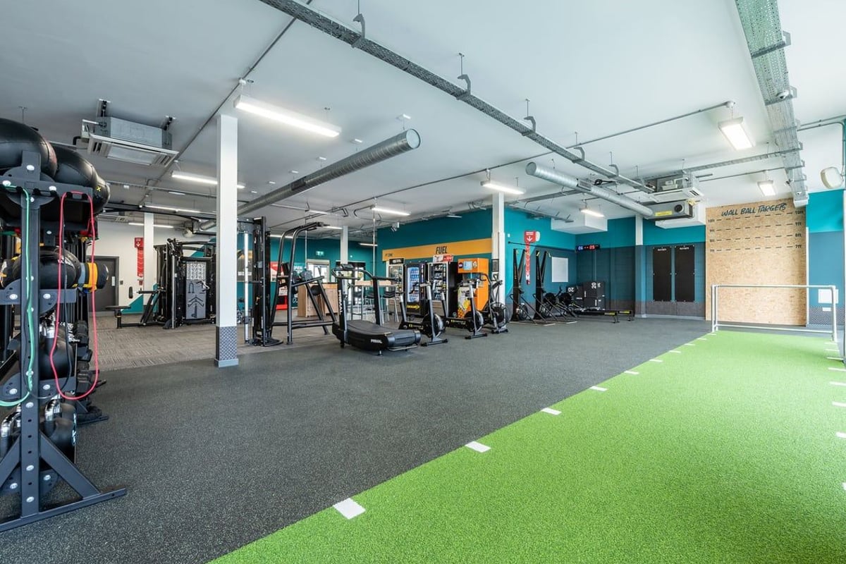 PureGym Wirral Bidston Moss: Weight training area with cable machines, squat racks, turf zone, rubberized flooring.