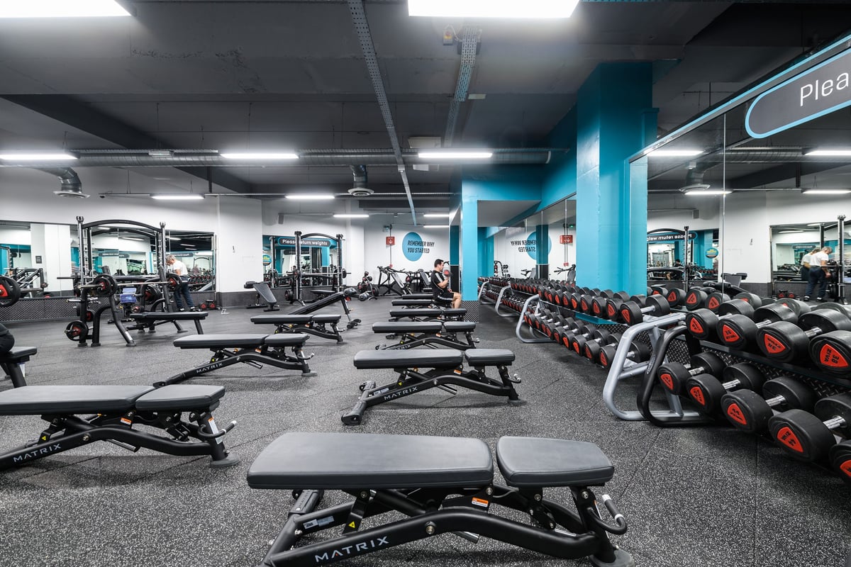 PureGym Bournemouth The Triangle: Rows of weight benches, dumbbells, and weight plates on rubberized gym flooring.